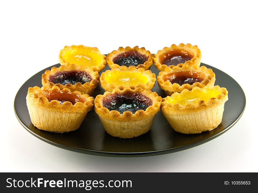 Selection red and yellow small jam tarts on a black plate with  a white background