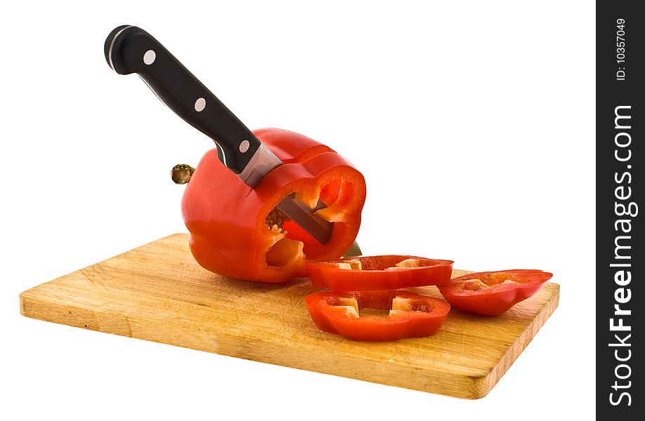 The knife cuts a fruit of red pepper on a chopping board on a white background. The knife cuts a fruit of red pepper on a chopping board on a white background
