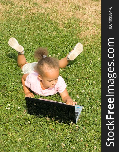 Beautiful young mixed race girl using laptop on a field of green grass and daisy wheel and clovers. She has the expression of contemplating what she is looking at on the display as she surfs the internet.