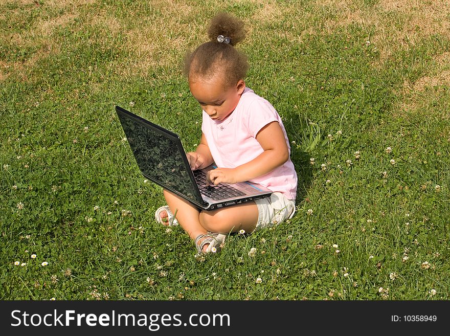 Beautiful young mixed race girl using laptop on a field of green grass and daisy wheel and clovers. She has the expression of contemplating what she is looking at on the display as she surfs the internet.