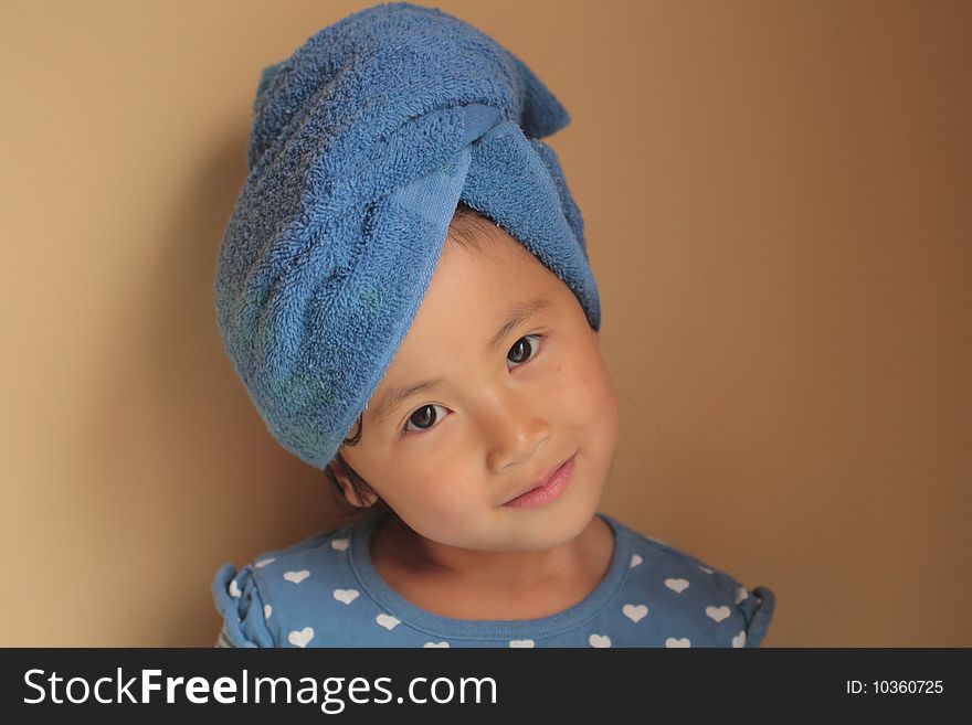 Closeup of a little girl of Asian descent, her hair wrapped in a blue bath towel. Isolated against a beige background. Closeup of a little girl of Asian descent, her hair wrapped in a blue bath towel. Isolated against a beige background.