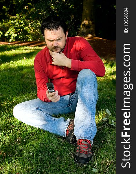 Pensive man with cellphone in park on summer day.