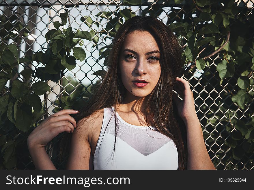 Woman in White Tank Top Standing Near Gray Metal Wire Fence