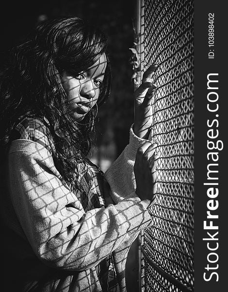 Grey Scale Photography Of Woman Standing Against Mesh Grill