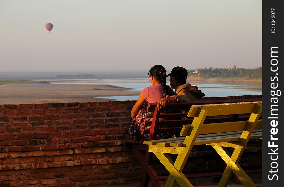 Couple siting in a bench watching the sunset with a ballon in the sky, city of Bagan, Myanmar (Burma)