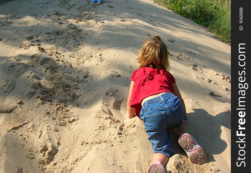 A toddler climbing a steep sand dune on a sunny day. A toddler climbing a steep sand dune on a sunny day