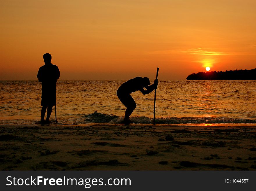 Two boys cleaning a beach, at sunset time. Two boys cleaning a beach, at sunset time