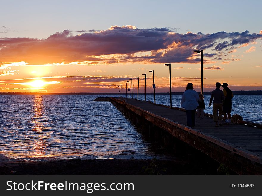 Various people enjoy a walk along a pier at sunset. Various people enjoy a walk along a pier at sunset.