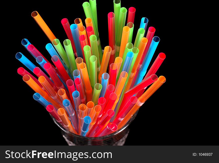 Close-up of vibrant colored straws in clear glass on black background. Close-up of vibrant colored straws in clear glass on black background