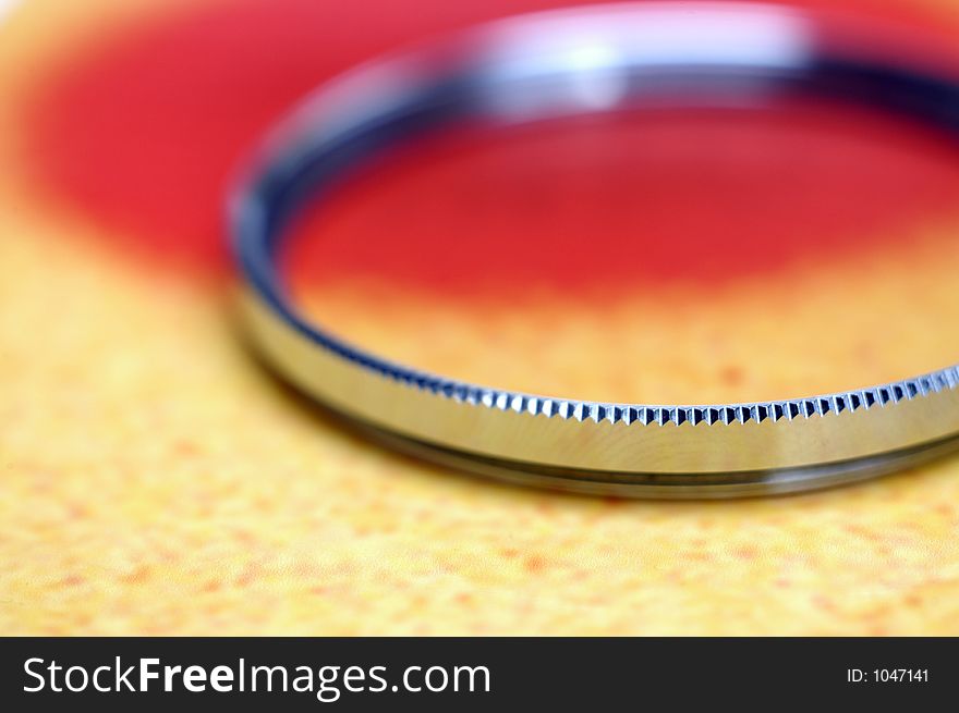 A shiny camera filter in shallow DoF on a colorful photographic print. A shiny camera filter in shallow DoF on a colorful photographic print