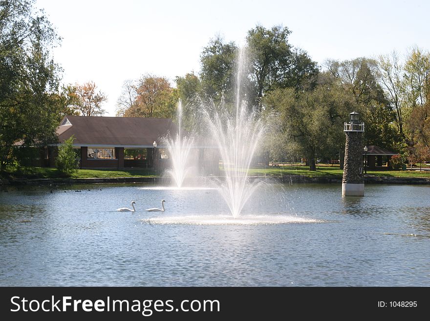 Two fountains and lighthouse in park pond on breezy day. Two fountains and lighthouse in park pond on breezy day.