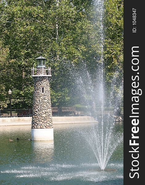 Lighthouse and fountain in pond on sunny day. Lighthouse and fountain in pond on sunny day.