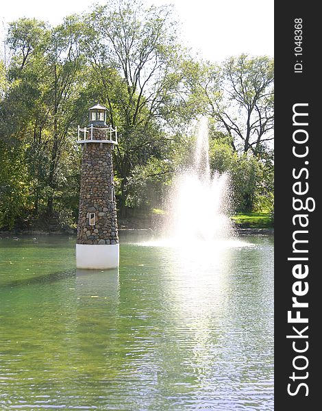 Lighthouse and fountain in pond on sunny day. Lighthouse and fountain in pond on sunny day.