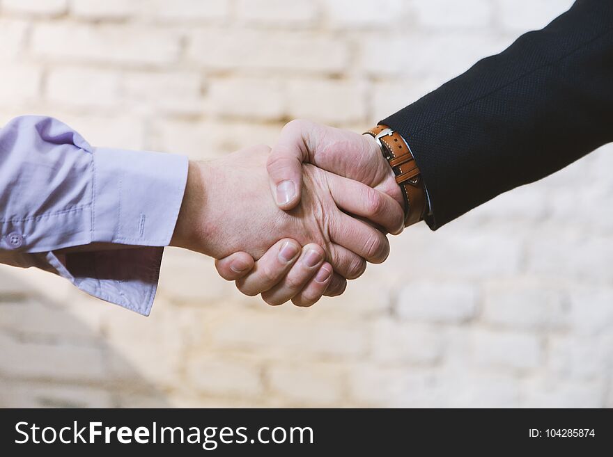 Business deal between two business man giving handshake together in front of brick wall background