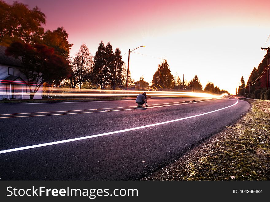 Person Sitting on Black Top Road during Twilight