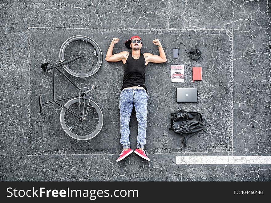 Man in Black Tank Top Laying on Gray Concrete Surface Near Black Bike
