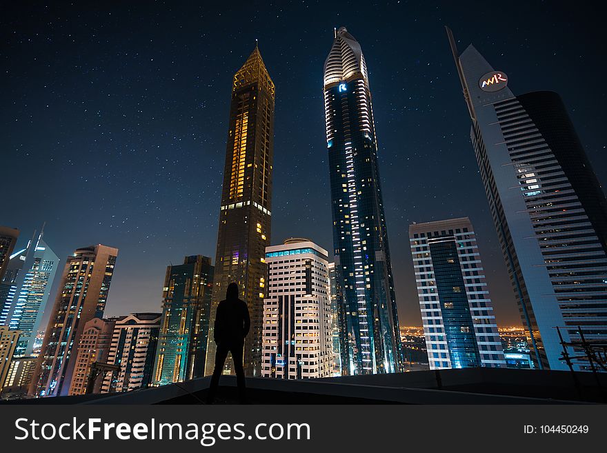 Man Standing In Assorted Building String Light During Night Time