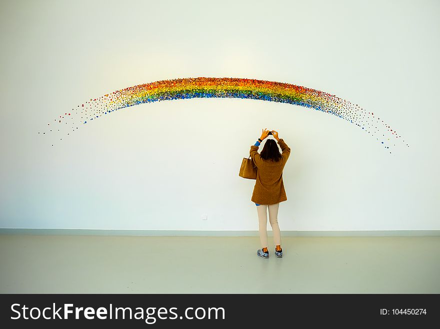 Woman Wearing Brown Top And Beige Leggings Taking Picture Rainbow Painted Wall