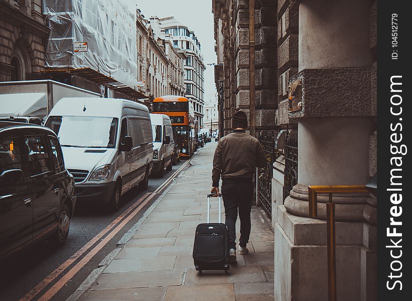 Man In Brown Jacket Holding Black Travel Luggage