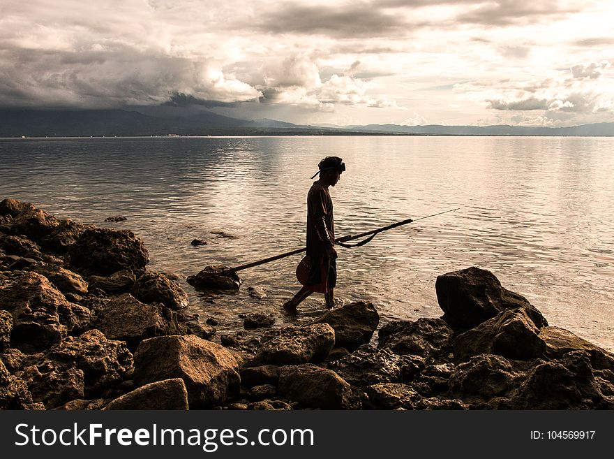 Person Holding Spear Beside Body of Water