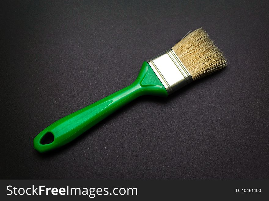 Closeup of green paintbrush at black paper background