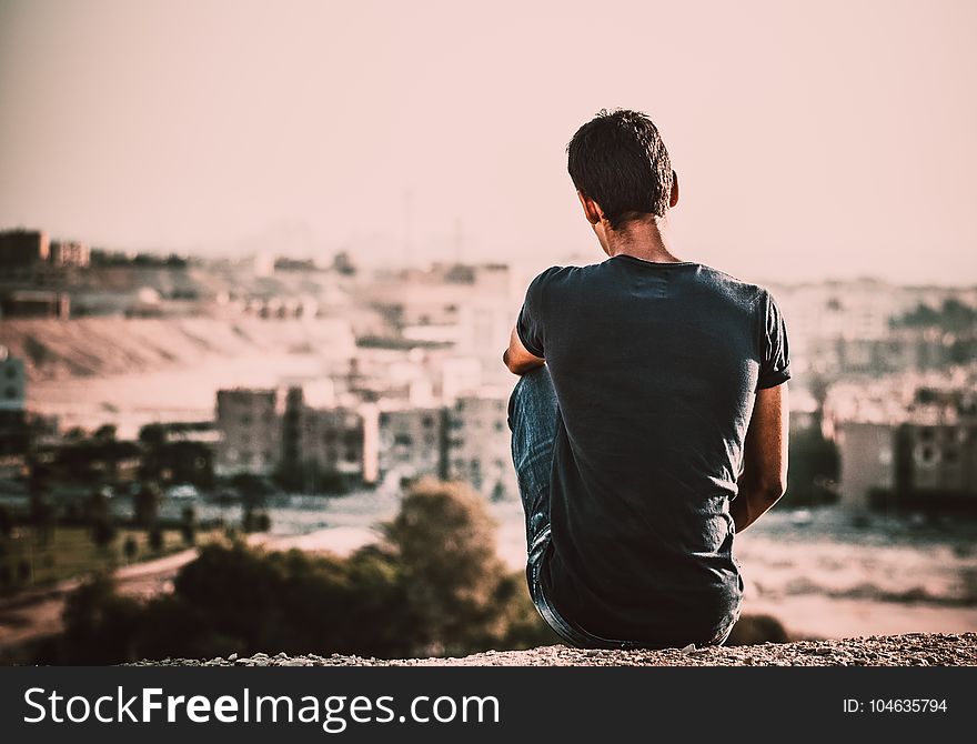 Man In Black Shirt And Blue Denim Jeans Sitting On Gray Stone At Daytime