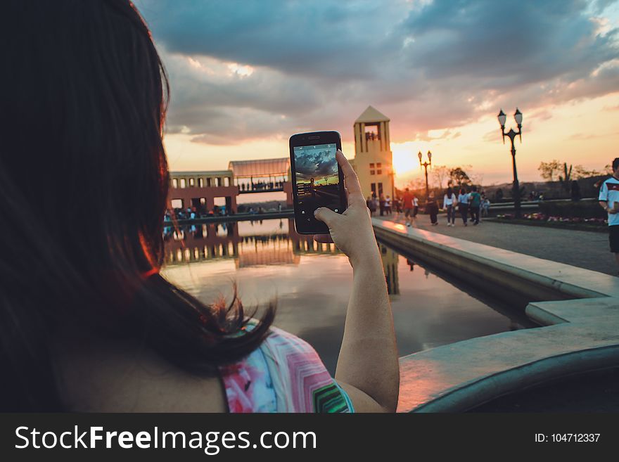 Woman Holding Smartphone Capturing Sunset