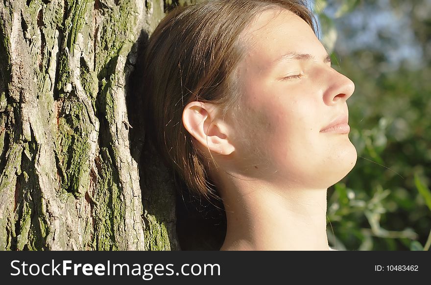 Girl with eyes closed leaned on the old tree with a ridge texture; young beautiful face with perfect springy skin. Girl with eyes closed leaned on the old tree with a ridge texture; young beautiful face with perfect springy skin