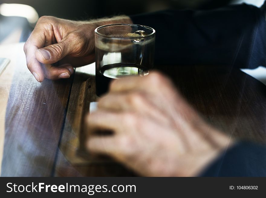 Man In Blue Long Sleeve Shirt In Front Of Drinking Glass On Brown Wooden Table