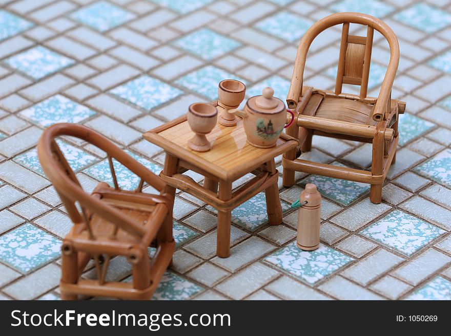 Toy tea set on rattan table, two chairs and hot water flask. Toy tea set on rattan table, two chairs and hot water flask