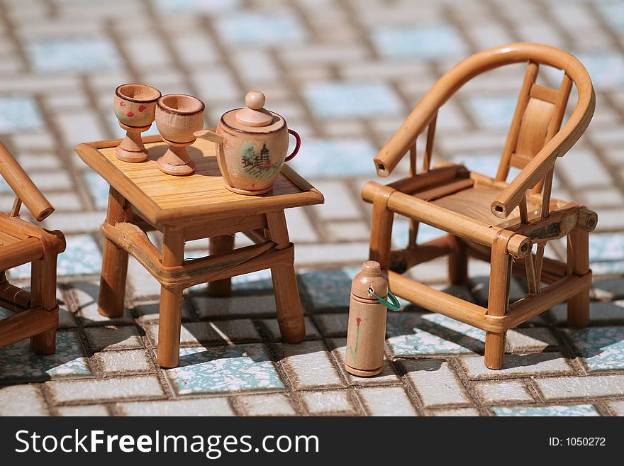 Toy tea set on rattan table, two chairs and hot water flask. Toy tea set on rattan table, two chairs and hot water flask