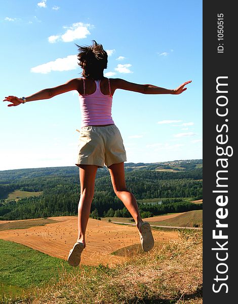 A young girl jumping up, beautiful country view in background. A young girl jumping up, beautiful country view in background