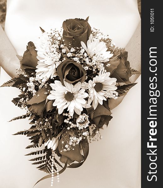 Bride holding her wedding bouquet against her dress, sepia