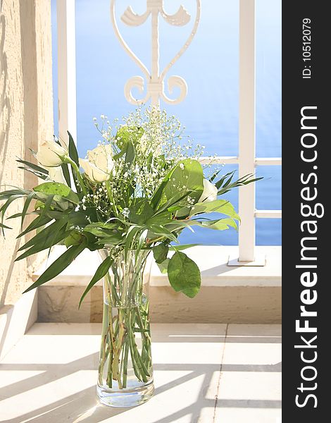 White roses in a glass vase, with blue morning sea on background