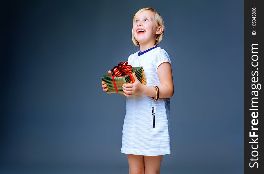 Modern Girl. happy trendy child in white dress isolated on grey background with Christmas present box looking on copy space. Modern Girl. happy trendy child in white dress isolated on grey background with Christmas present box looking on copy space