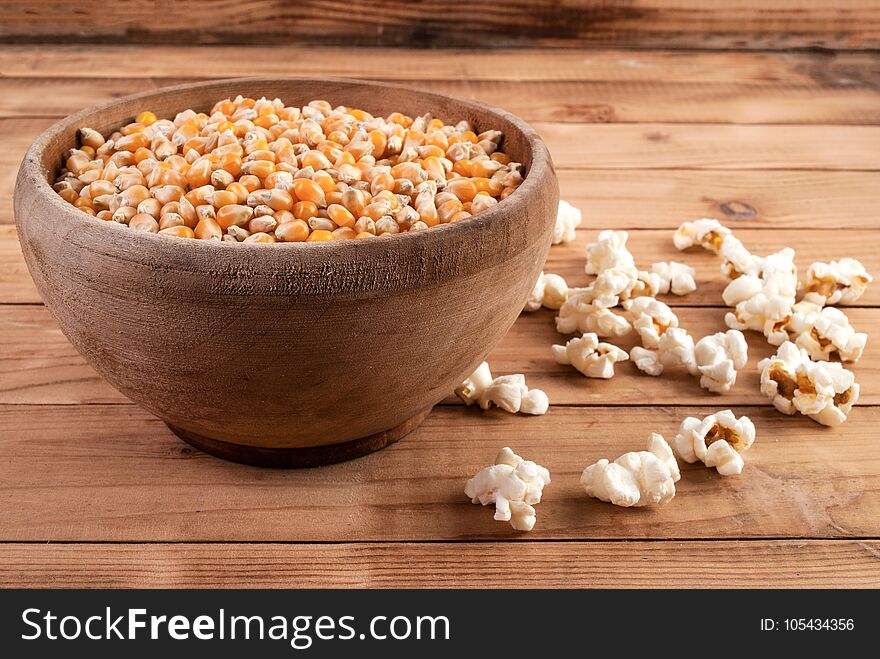 Raw corn seeds in wooden bowl and popped popcorn on table