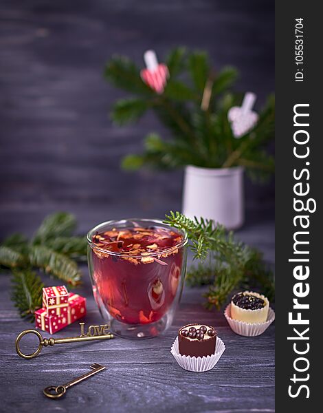 Fruit and hibiscus tea in transparent cup, luxury chocolates candy and christmas tree branch on a dark wooden background