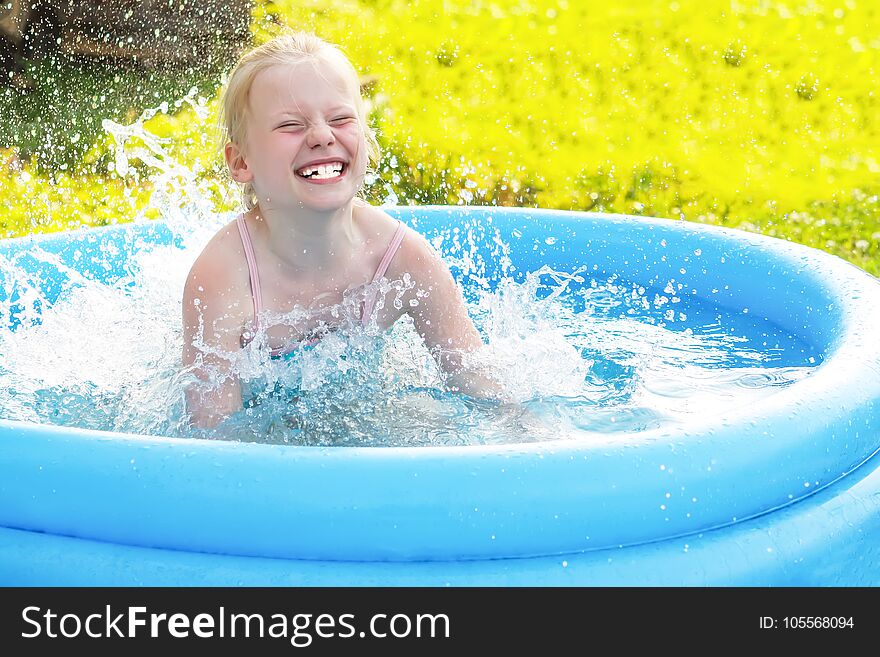 Little blonde girl playing in outdoor swimming pool on hot summer day.