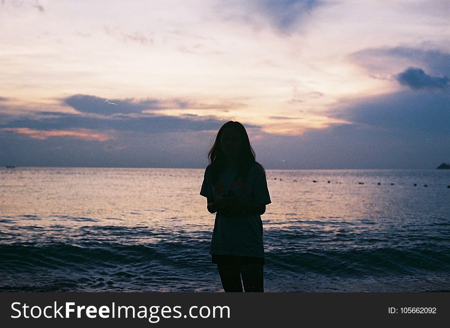 Silhouette of Woman Standing Near Large Body of Water