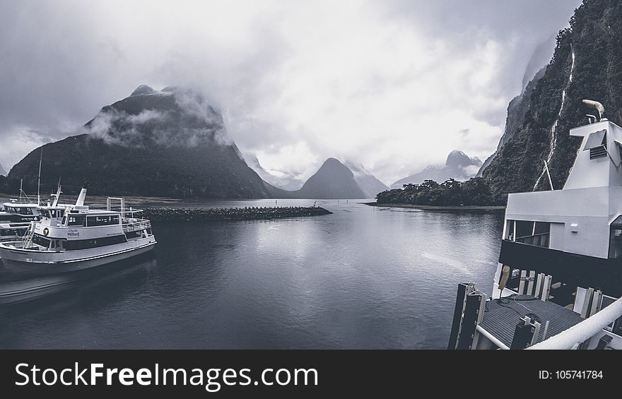 Grayscale Photo of Yachts on Body of Water Under Cloudy Sky