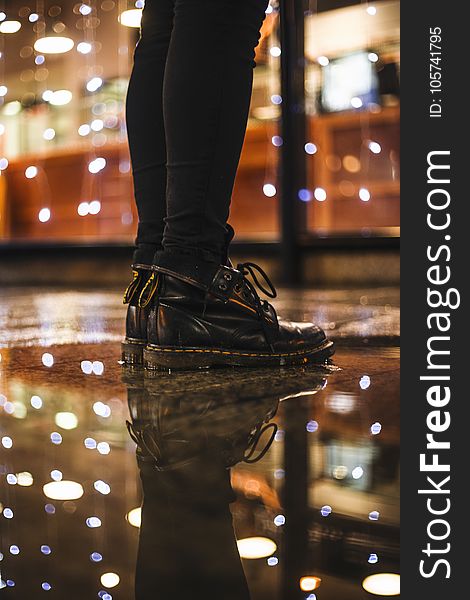 Photo of Person Wearing Black Fitted Jeans and Black Dr.martens Boots Standing on Black Floor Tiles