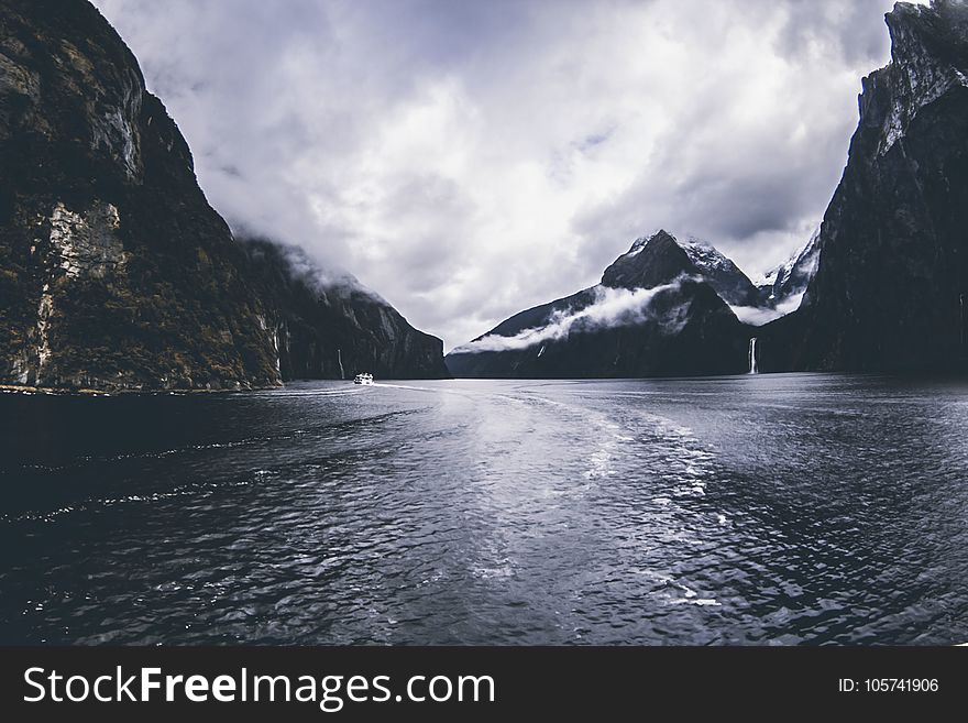 Body of Water Surround by Mountains Under Cloudy Sky