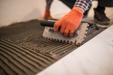 Free Laying Ceramic Tiles. Troweling Mortar Onto A Concrete Floor In Preparation For Laying White Floor Tile. Royalty Free Stock Photo - 105816595