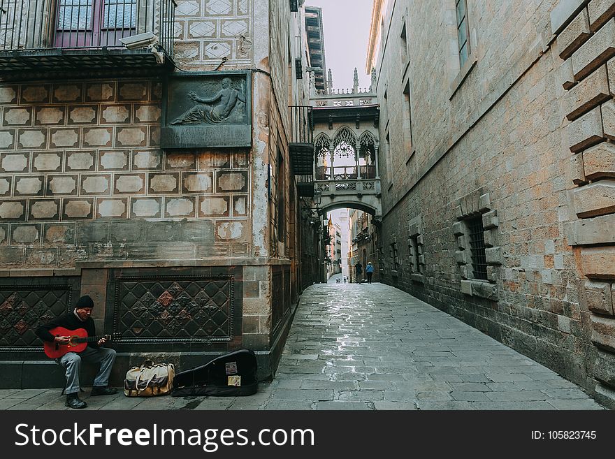 Man Playing Guitar Beside Brown Concrete Wall Next To Hallway