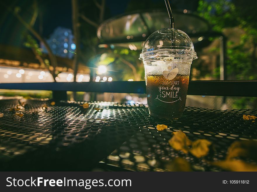 Clear Plastic Disposable Cup With Straw Half-filled With Juice on Metal Table