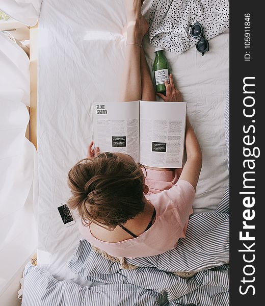 Woman in Pink Dress Sitting on Bed While Reading