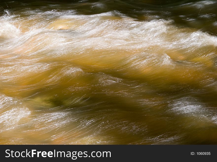 Hues of green and gold along with light trails from the reflection of the sun in flowing water. Hues of green and gold along with light trails from the reflection of the sun in flowing water