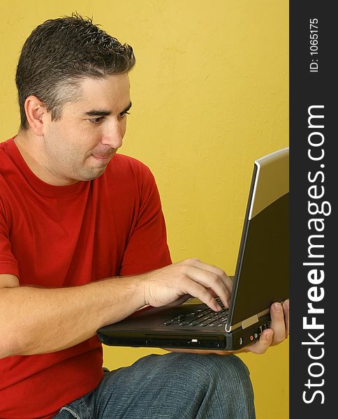 Thirty-two year old man with laptop against yellow wall.