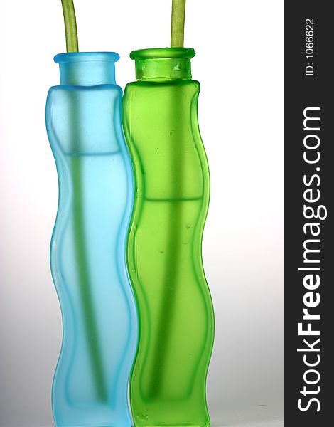 Blue and green translucent glass vases with water and stem against white background. Blue and green translucent glass vases with water and stem against white background