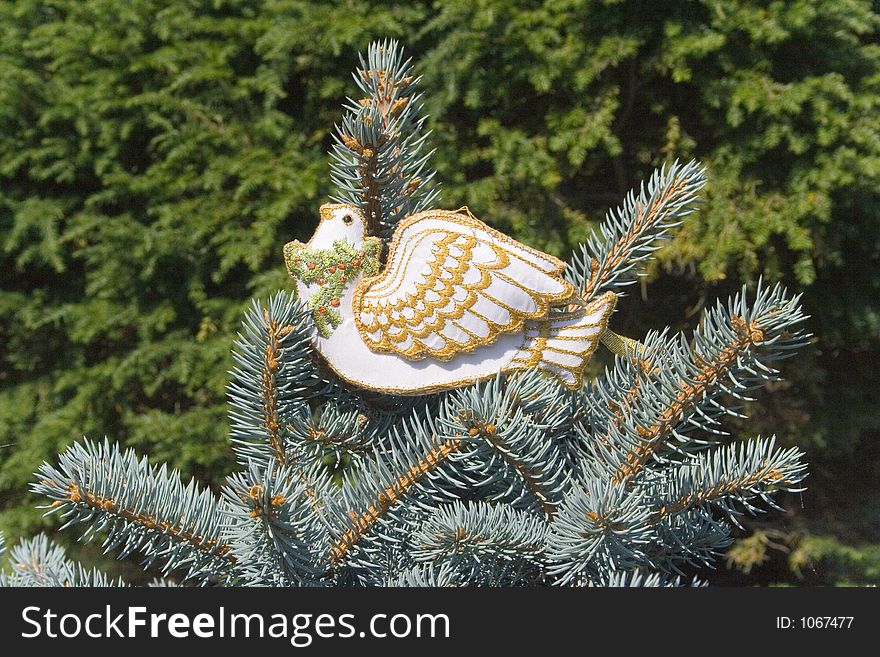 The Dove of Peace rests atop the uppermost branches of a christmas tree. Beautifully embroidered with gold thread, a wreath of holly with red berries adorns it's neck. The Dove of Peace rests atop the uppermost branches of a christmas tree. Beautifully embroidered with gold thread, a wreath of holly with red berries adorns it's neck.